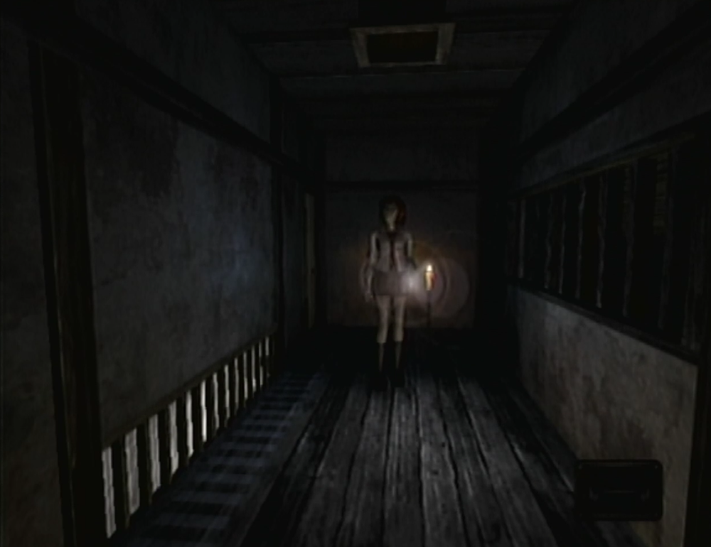 A screenshot from Fatal Frame, where the player-controlled character, Miku, is facing the camera from the other side of a dark hallway.